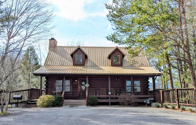 log-style house with covered porch, metal roof, a chimney, and log siding