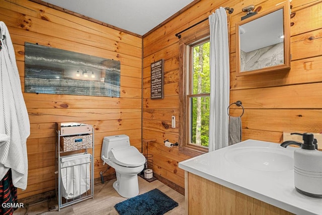 bathroom featuring wooden walls, toilet, wood finished floors, and vanity