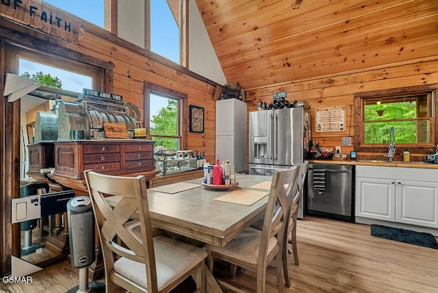 dining area with plenty of natural light, wooden walls, light wood-style flooring, and high vaulted ceiling