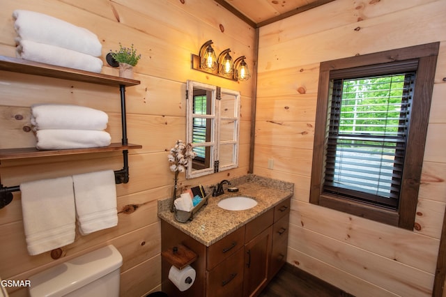 bathroom featuring wooden walls, vanity, toilet, and a healthy amount of sunlight
