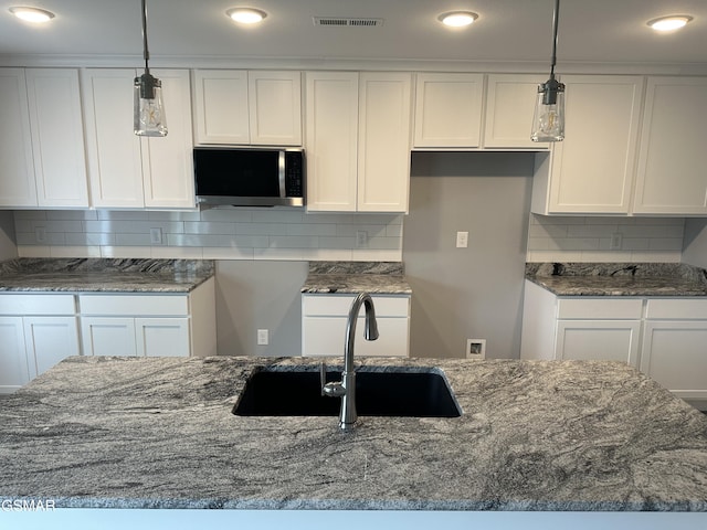 kitchen featuring visible vents, stainless steel microwave, decorative light fixtures, and white cabinets