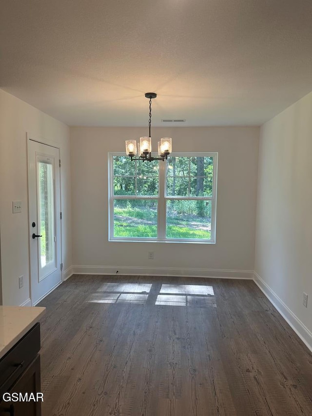 unfurnished dining area with dark wood-style flooring, visible vents, a notable chandelier, and baseboards