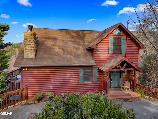 log home featuring roof with shingles, a chimney, and fence