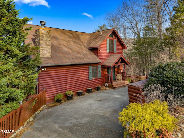 log cabin featuring a chimney, a shingled roof, fence, log veneer siding, and driveway