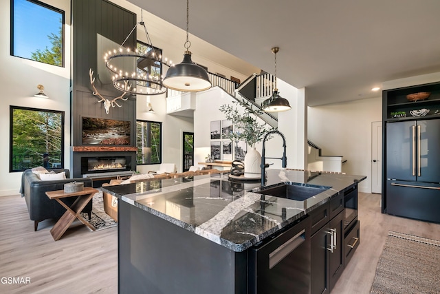 kitchen with built in fridge, a sink, dishwasher, dark stone countertops, and a glass covered fireplace