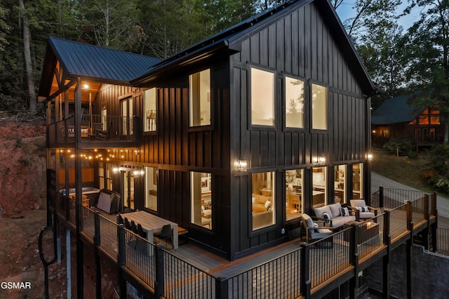 rear view of house featuring board and batten siding, metal roof, and a balcony