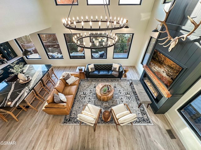 living area with visible vents, a high ceiling, wood finished floors, a chandelier, and baseboards