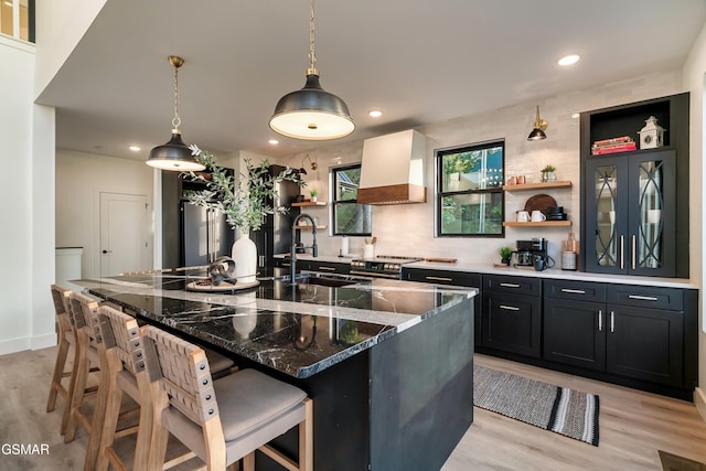 kitchen featuring light wood-style floors, premium range hood, open shelves, and a sink