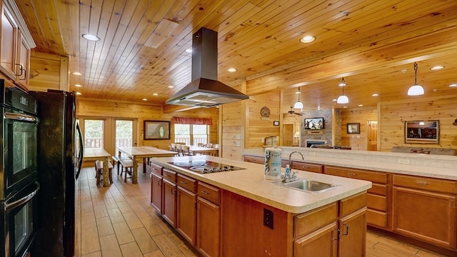 kitchen featuring island exhaust hood, sink, black appliances, pendant lighting, and an island with sink