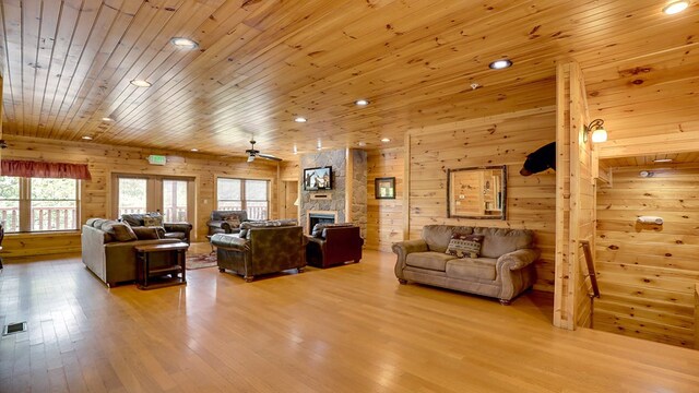 living room with wood ceiling, ceiling fan, a fireplace, light hardwood / wood-style floors, and wood walls