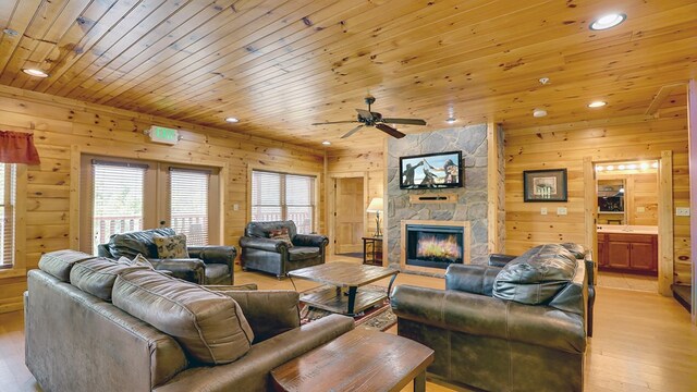 living room with ceiling fan, wooden ceiling, wooden walls, a fireplace, and light wood-type flooring