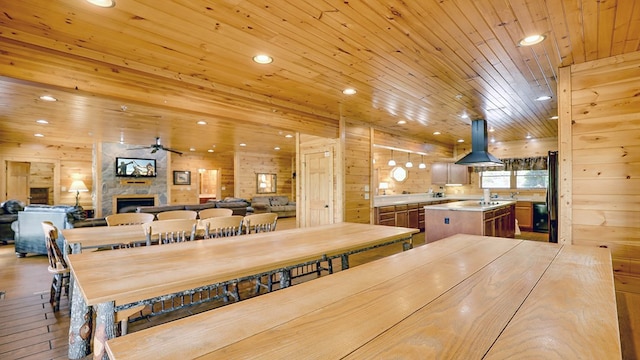 dining space featuring wood walls, a stone fireplace, ceiling fan, light hardwood / wood-style floors, and wood ceiling