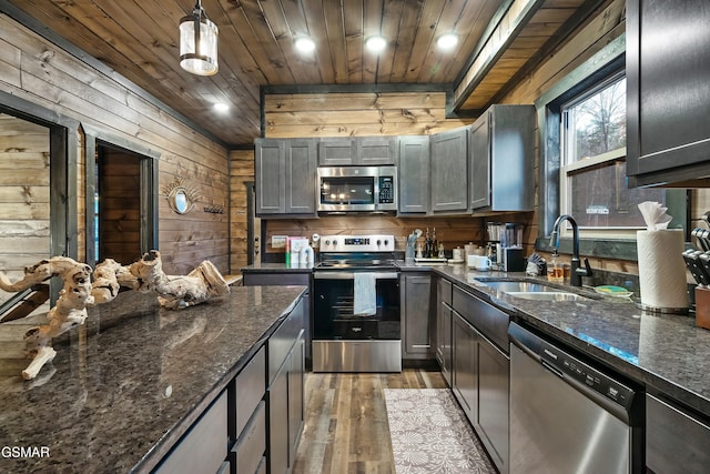 kitchen featuring stainless steel appliances, light wood-style floors, a sink, wooden walls, and wooden ceiling