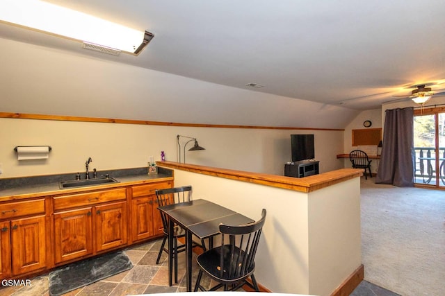 kitchen with ceiling fan, a kitchen breakfast bar, sink, light colored carpet, and vaulted ceiling