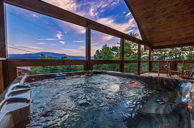 pool at dusk featuring a mountain view and a hot tub