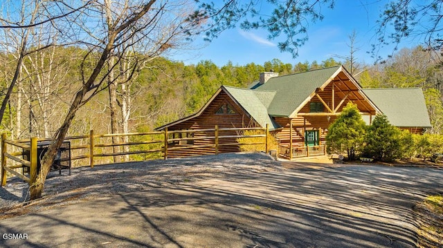 log-style house featuring log exterior, driveway, a chimney, and a view of trees