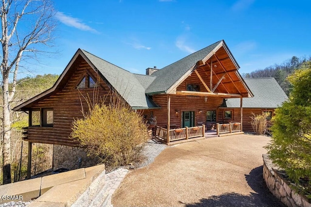 rear view of property with log exterior, a chimney, driveway, and roof with shingles