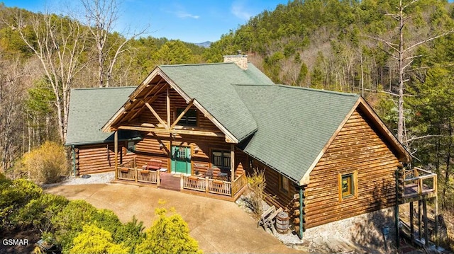 log home featuring log siding, a view of trees, a chimney, and a shingled roof