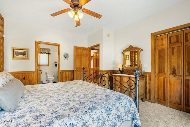 bedroom with a wainscoted wall, a ceiling fan, connected bathroom, carpet floors, and wood walls