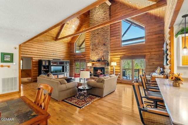 living area with visible vents, beam ceiling, a stone fireplace, a textured ceiling, and wood-type flooring