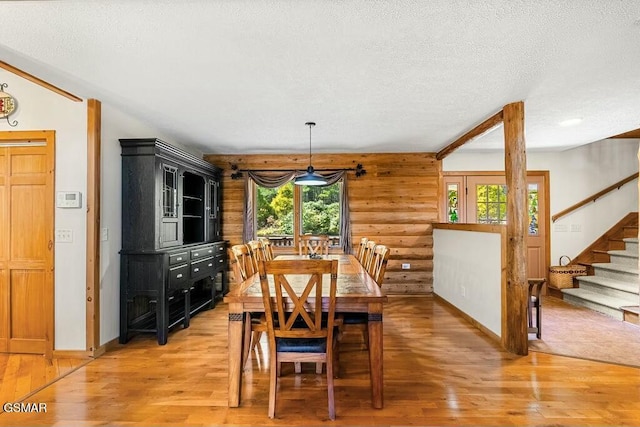 dining area featuring a textured ceiling, stairway, light wood finished floors, and rustic walls