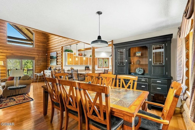 dining area featuring rustic walls, high vaulted ceiling, a textured ceiling, and light wood-style floors