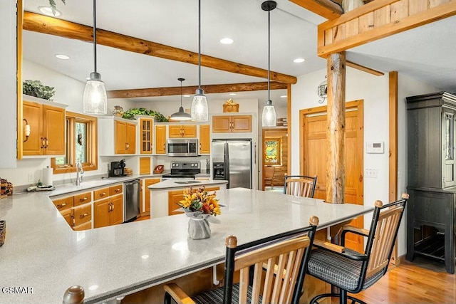 kitchen with beamed ceiling, a peninsula, stainless steel appliances, pendant lighting, and a kitchen breakfast bar