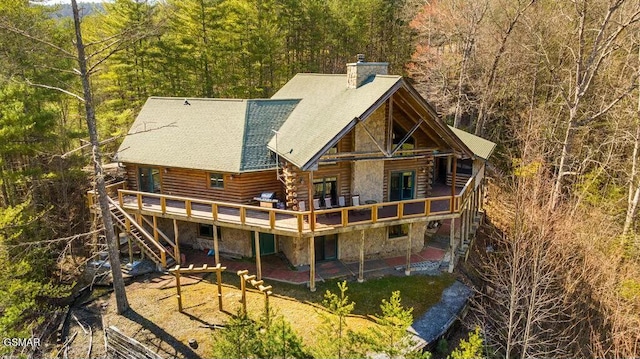 back of property featuring a wooded view, log exterior, a chimney, stone siding, and a patio