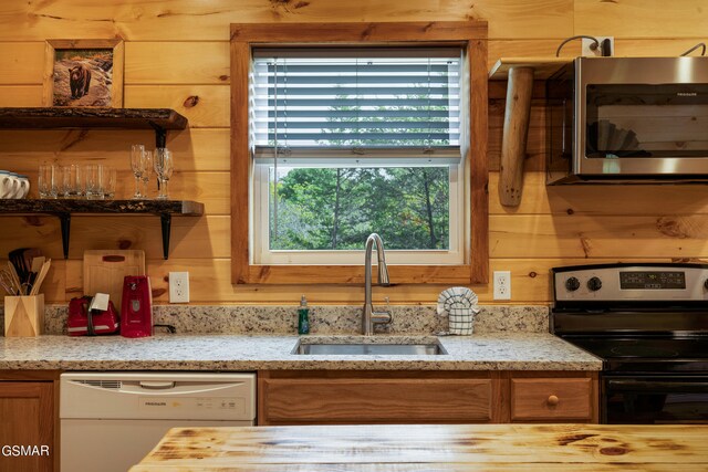 kitchen featuring dishwasher, wood walls, black range oven, sink, and light stone counters