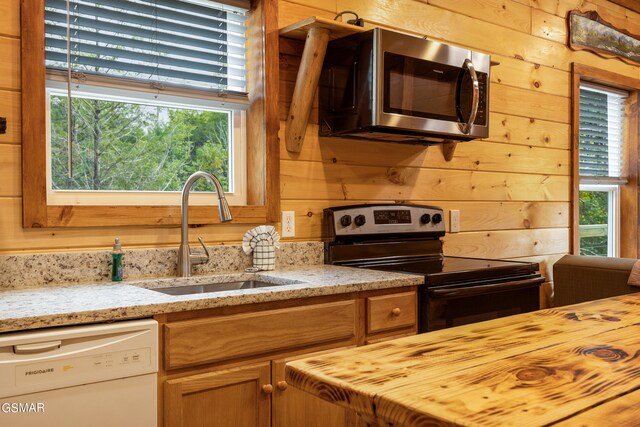 kitchen featuring light stone counters, sink, electric stove, dishwasher, and wood walls