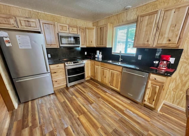 kitchen featuring appliances with stainless steel finishes, light wood-type flooring, light brown cabinetry, a textured ceiling, and sink