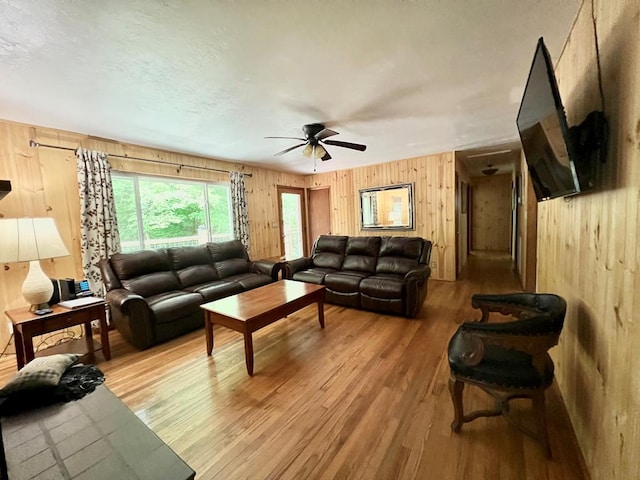 living room with hardwood / wood-style flooring, ceiling fan, and wood walls