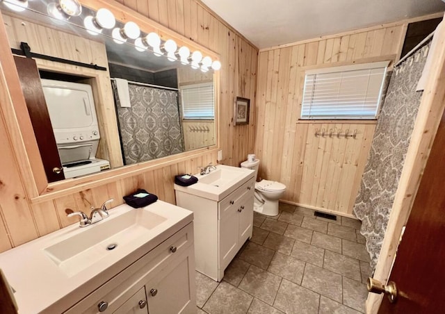 bathroom featuring vanity, toilet, stacked washer / dryer, and wooden walls