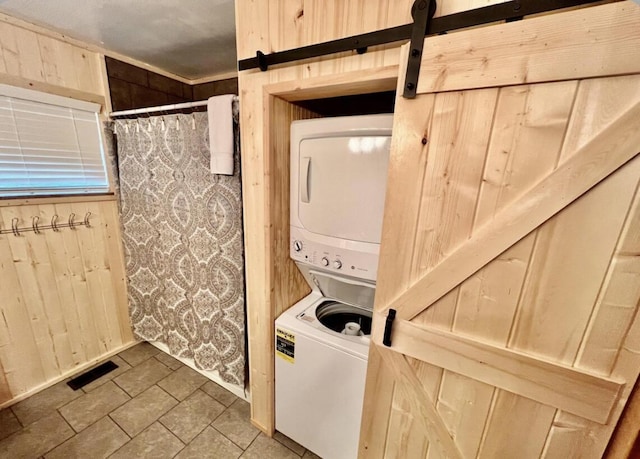 laundry room with tile patterned floors, a barn door, wood walls, and stacked washer / drying machine