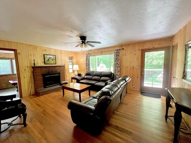 living room with ceiling fan, light wood-type flooring, a textured ceiling, and a brick fireplace