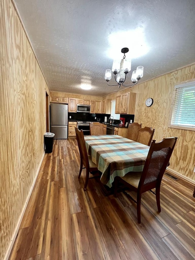 dining room with wooden walls, dark hardwood / wood-style flooring, a chandelier, and a textured ceiling