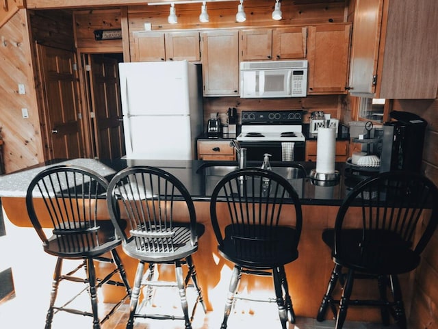 kitchen featuring a kitchen bar, white appliances, and wooden walls