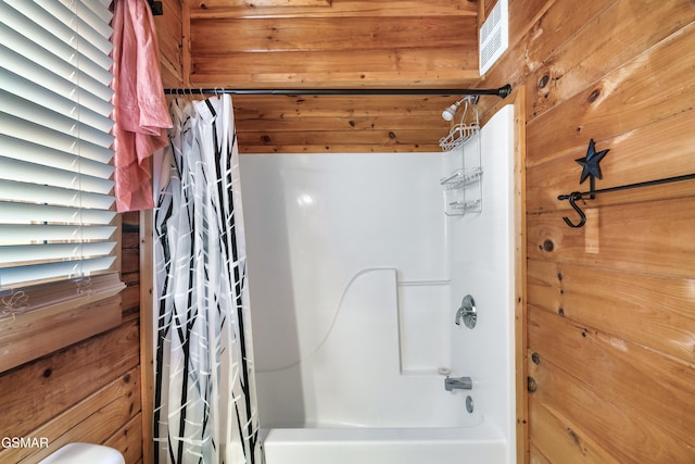 bathroom with shower / bath combo with shower curtain, a healthy amount of sunlight, and wooden walls