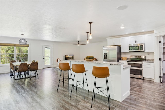 kitchen featuring a center island, white cabinets, stainless steel appliances, and decorative light fixtures