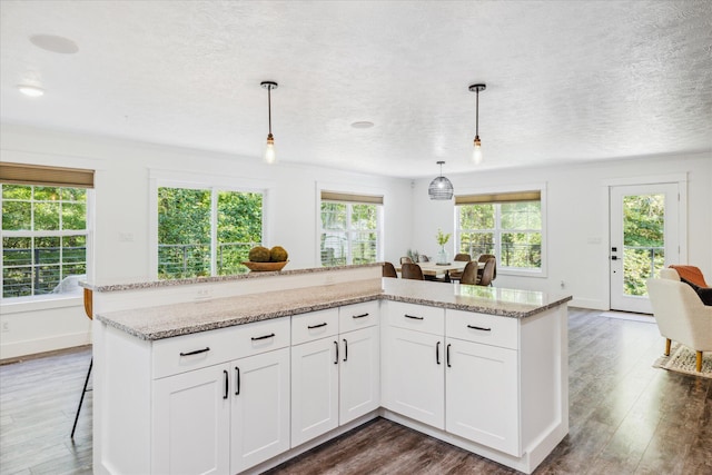 kitchen featuring white cabinets, decorative light fixtures, light stone counters, and a wealth of natural light