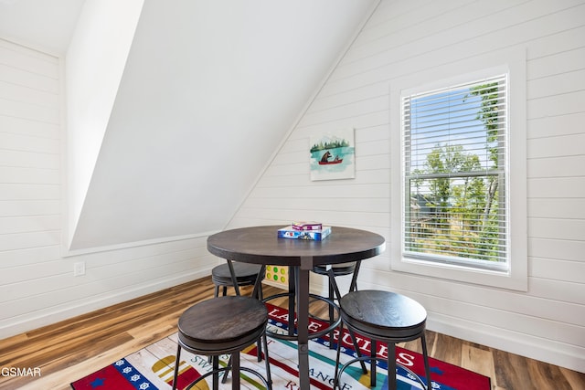 dining space with wood walls, hardwood / wood-style floors, a healthy amount of sunlight, and vaulted ceiling