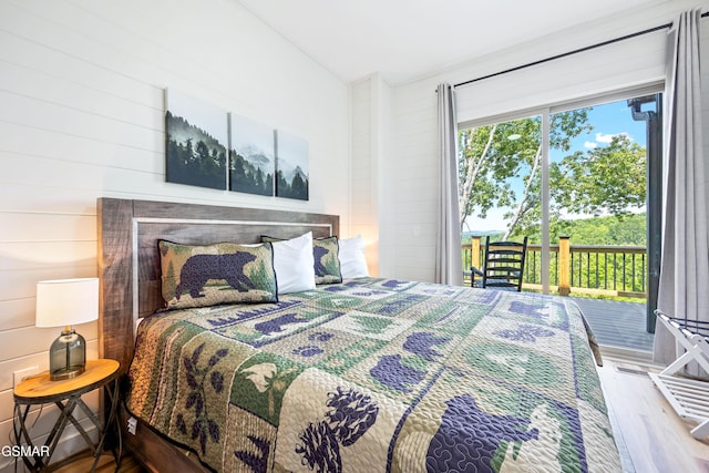 bedroom with access to exterior, wood-type flooring, and wooden walls