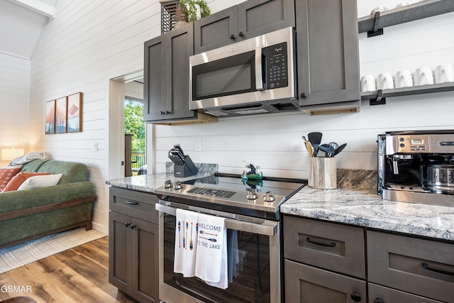 kitchen featuring stainless steel appliances, light stone counters, dark hardwood / wood-style flooring, lofted ceiling, and dark brown cabinets