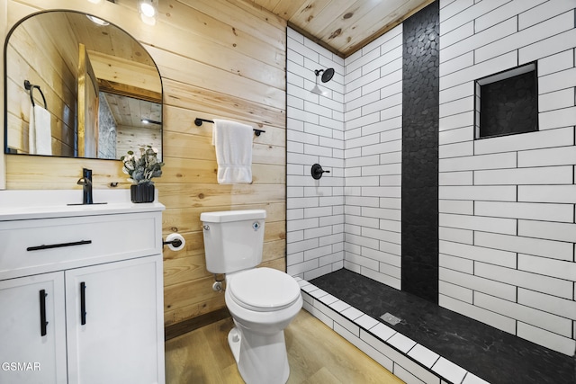 bathroom featuring toilet, wood finished floors, wood walls, tiled shower, and vanity