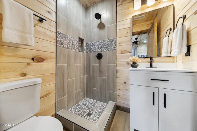 bathroom with tiled shower, toilet, wood walls, and vanity