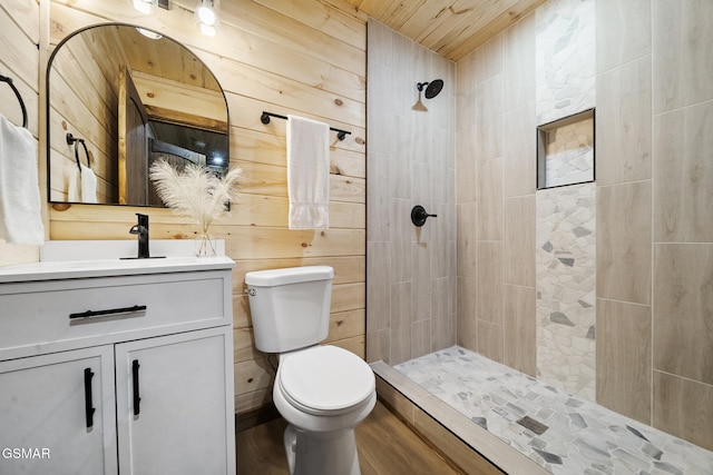 full bathroom featuring wooden walls, tiled shower, toilet, and vanity