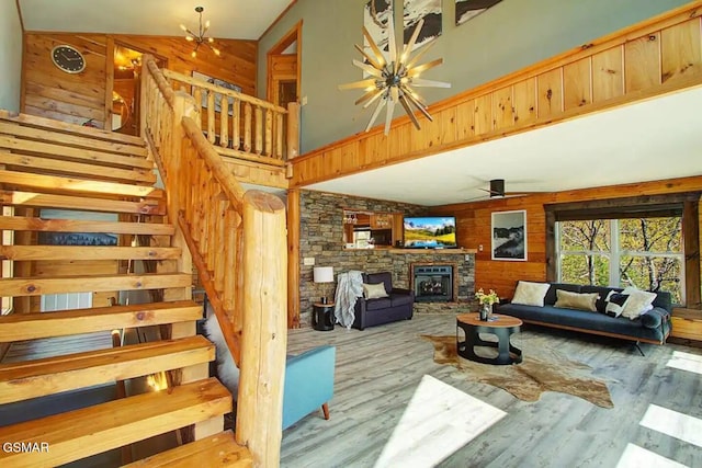 living area featuring stairway, wood finished floors, a fireplace, wood walls, and ceiling fan with notable chandelier