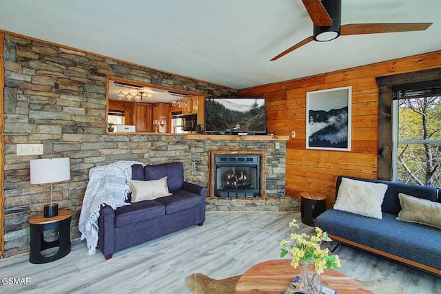 living area with a stone fireplace, wood finished floors, wood walls, and ceiling fan