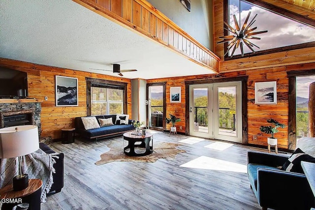 living room featuring a ceiling fan, a textured ceiling, wood finished floors, french doors, and wood walls