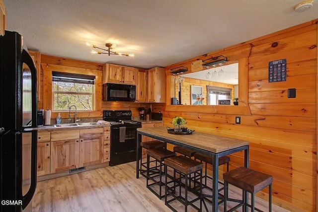 kitchen with visible vents, wood walls, light wood-style floors, black appliances, and a sink